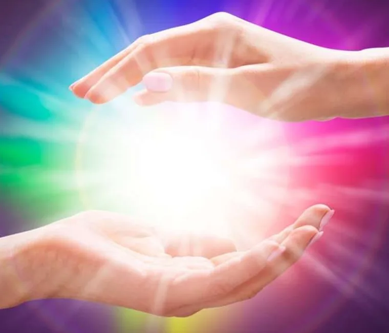 Mãos em gesto de Reiki com luz colorida